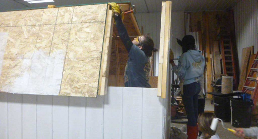 Two people work on a wooden structure during a service project with outward bound. 